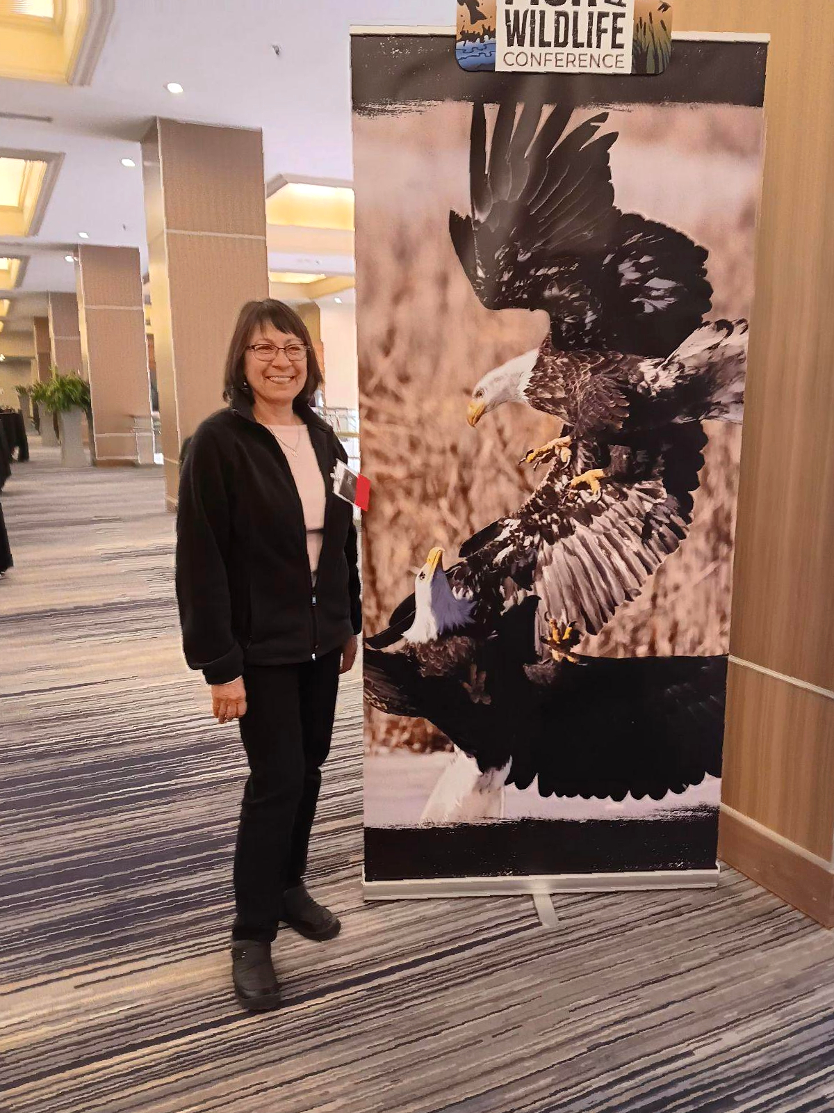 Dr. Nadia Navarrete-Tindall smiling next to a Wildlife Conference banner featuring a majestic eagle.