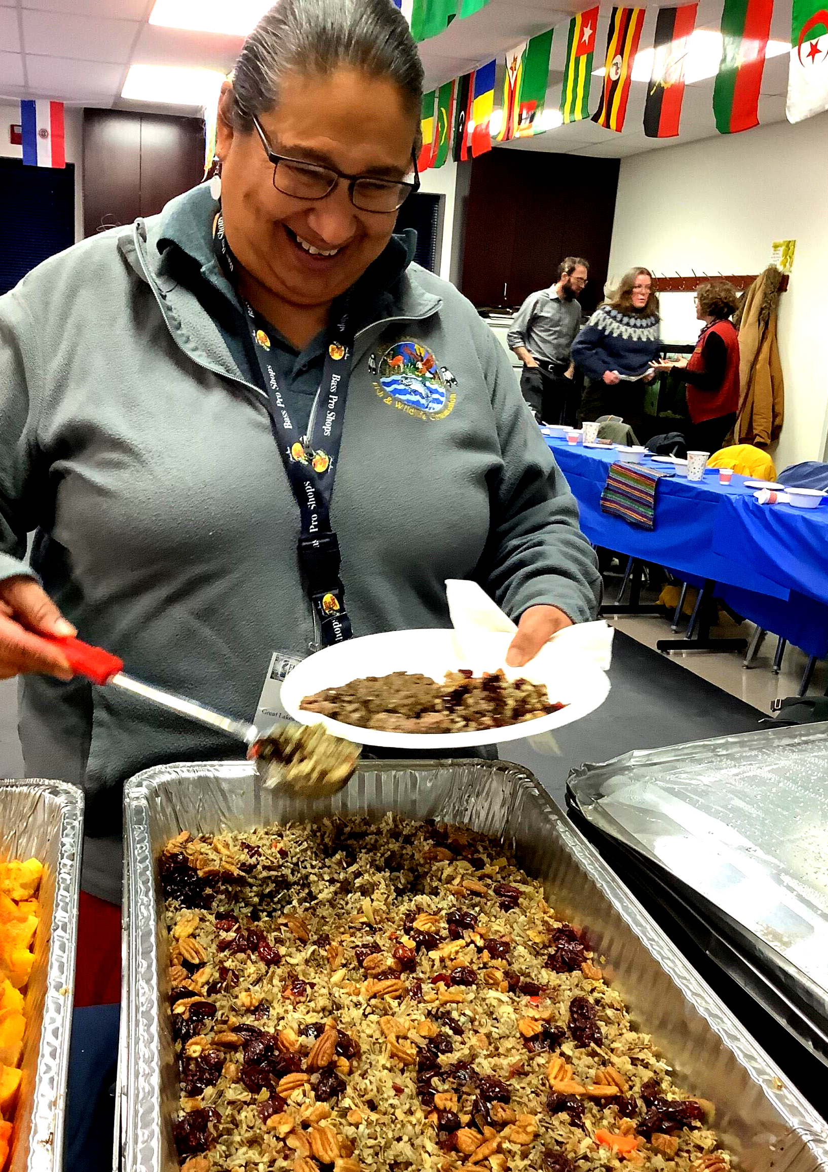 Woman serving a plate of wild rice with nuts and berries, smiling at a community event.