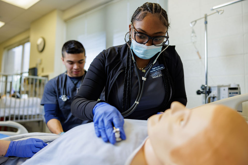 Two Lincoln University of Missouri nursing students practice by listening to the heartbeat of a practice dummy with a stethoscope.