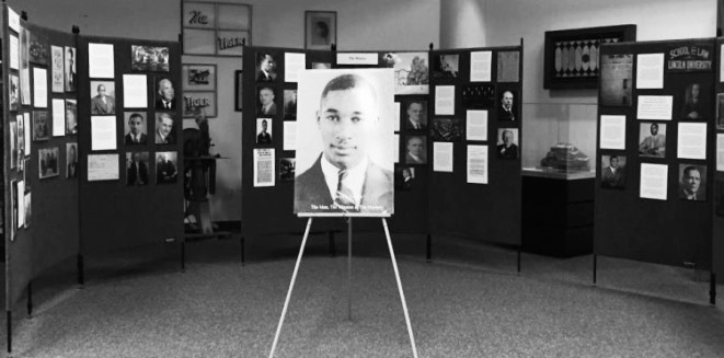 A Lloyd Gaines pictures sits on an easel in the center of a room in the library. The walls are filled with photos from the Lloyd Gaines exhibit. 