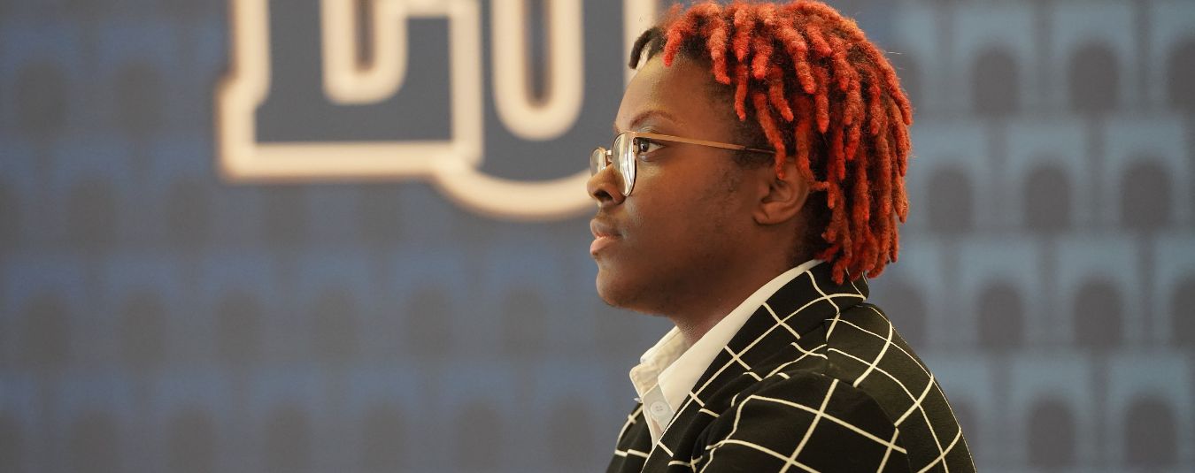 A graduate student in professional dress listens to a speaker