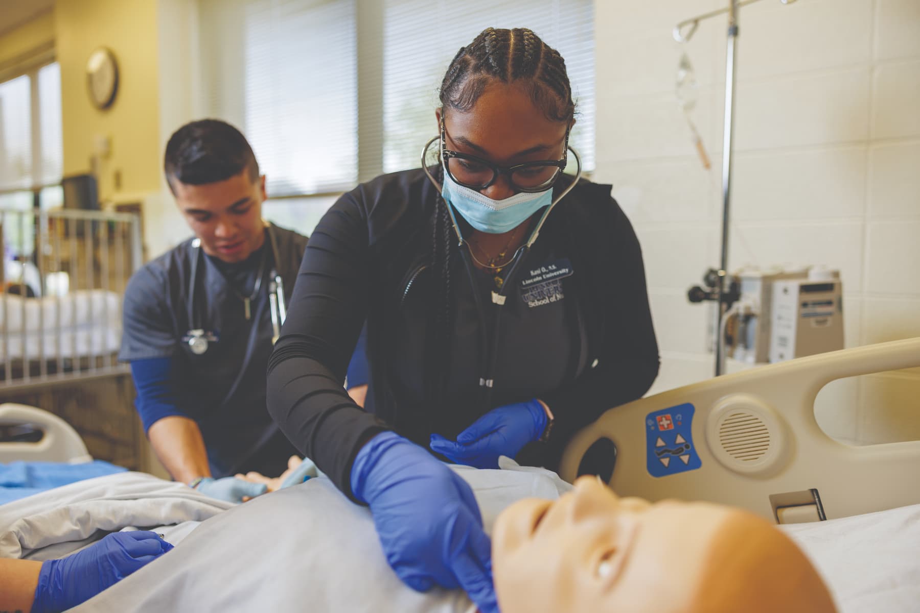 Young Black female nursing student assesses a simulation manikin while a male student stands behind