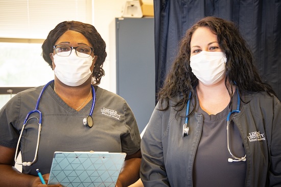 Two women in scrubs from Lincoln University of Missouri School of Nursing, holding papers and wearing masks, collaborating together.